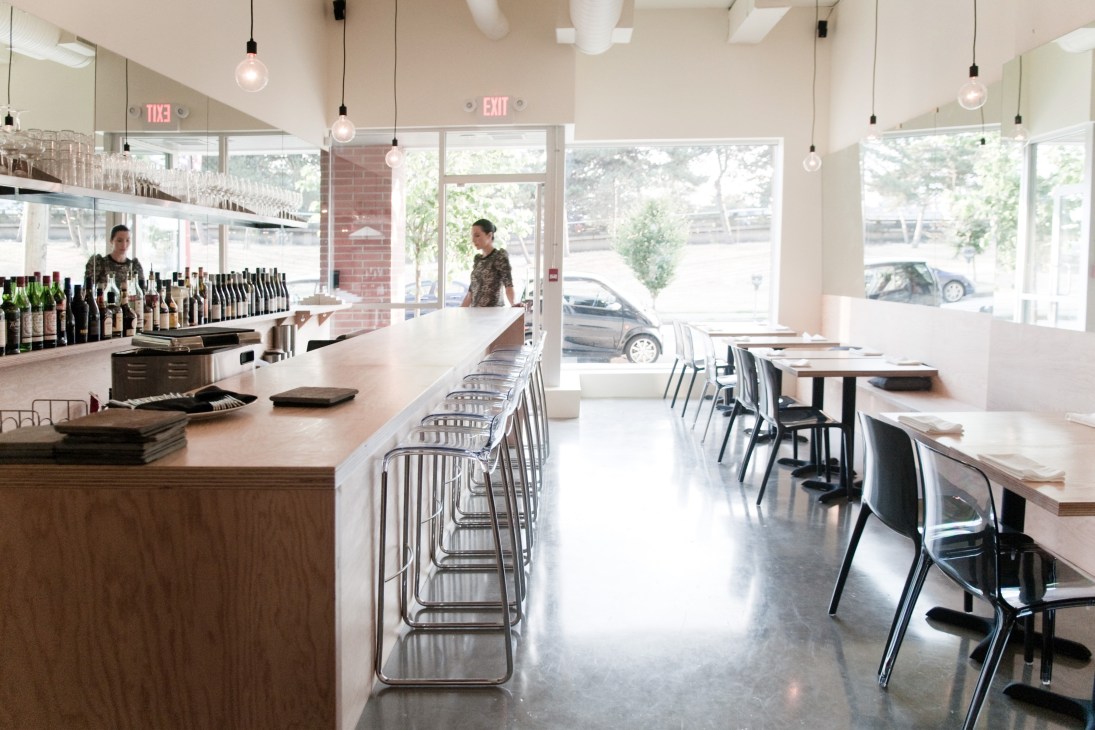 Interior of The Parker restaurant with counter seating, wine bottles on display, and dining tables near large windows.