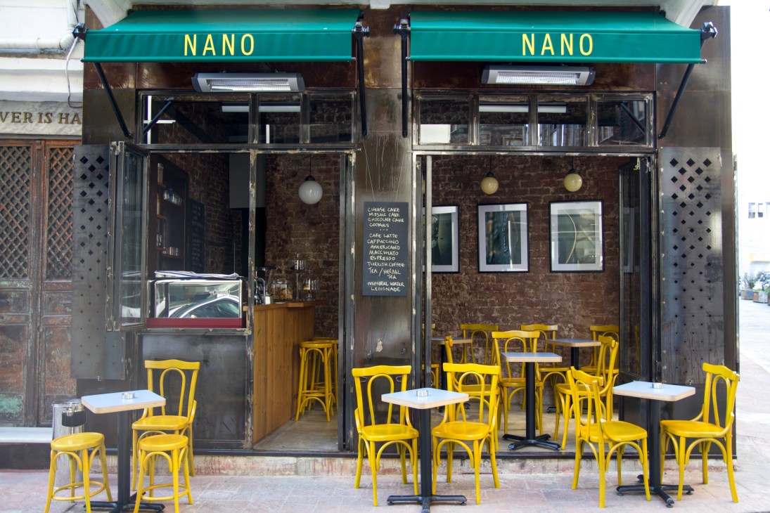 Nano café storefront with turquoise awning, dark brick façade, and bright yellow bentwood chairs outside.