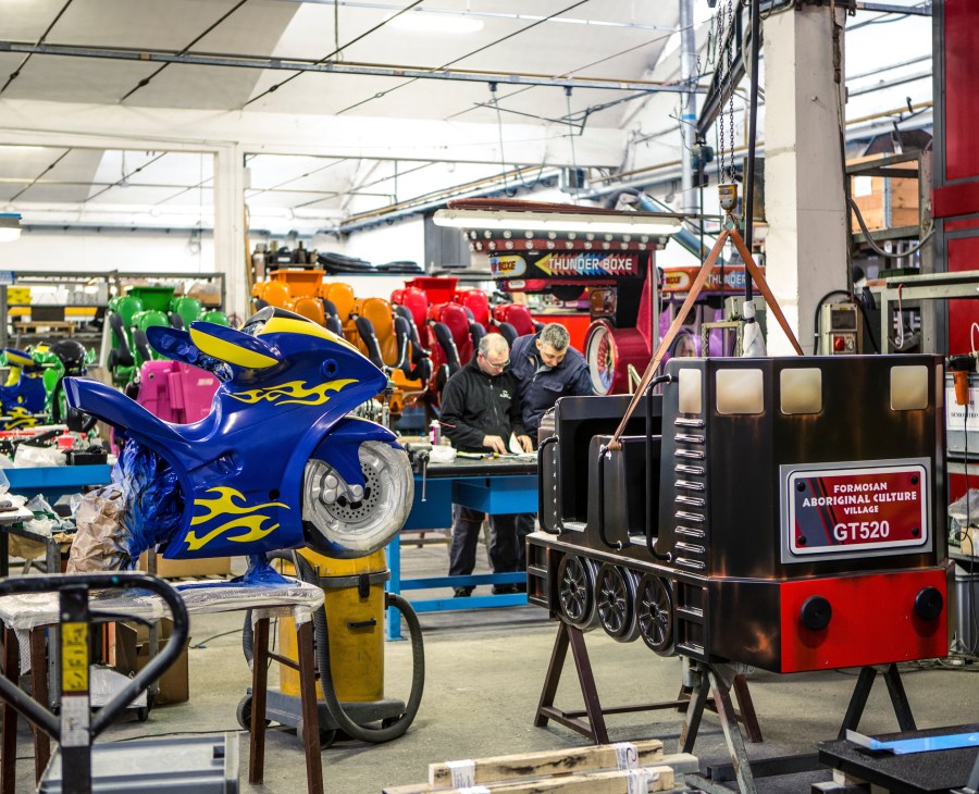 Inside the Zamperla factory with ride components in various stages of assembly and workers in the background.