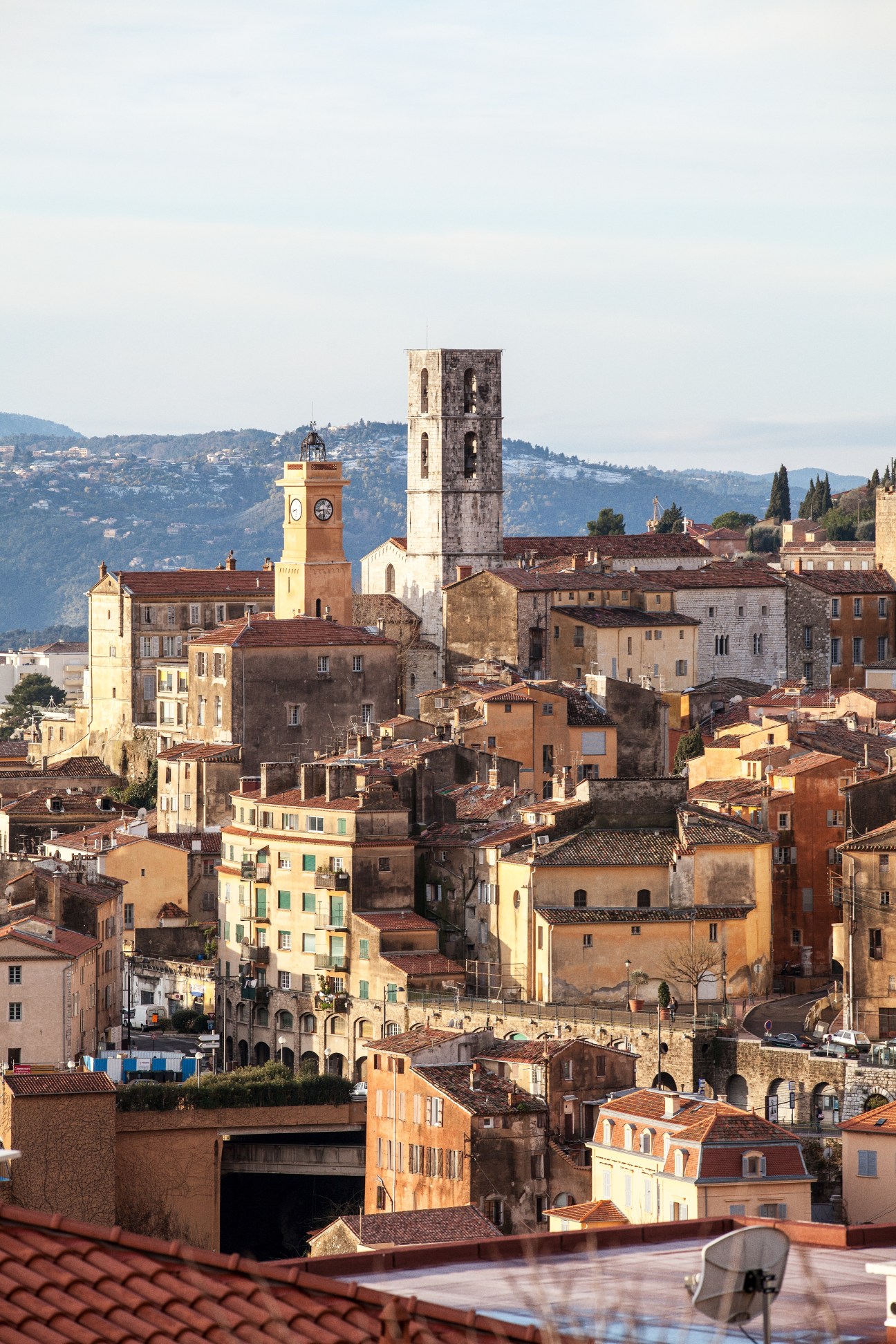 Hilltop town of Grasse with historic buildings, church towers, and Mediterranean landscape in background.