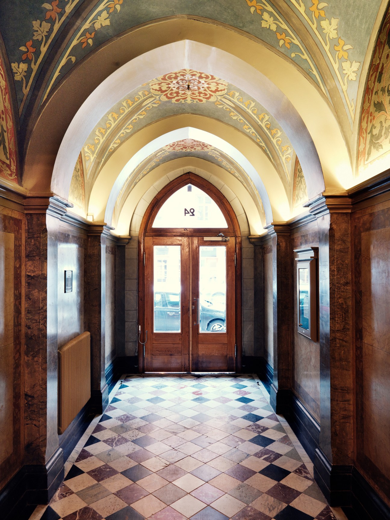 Ornate arched entryway with decorative painted ceiling, wooden doors, and patterned floor tiles.