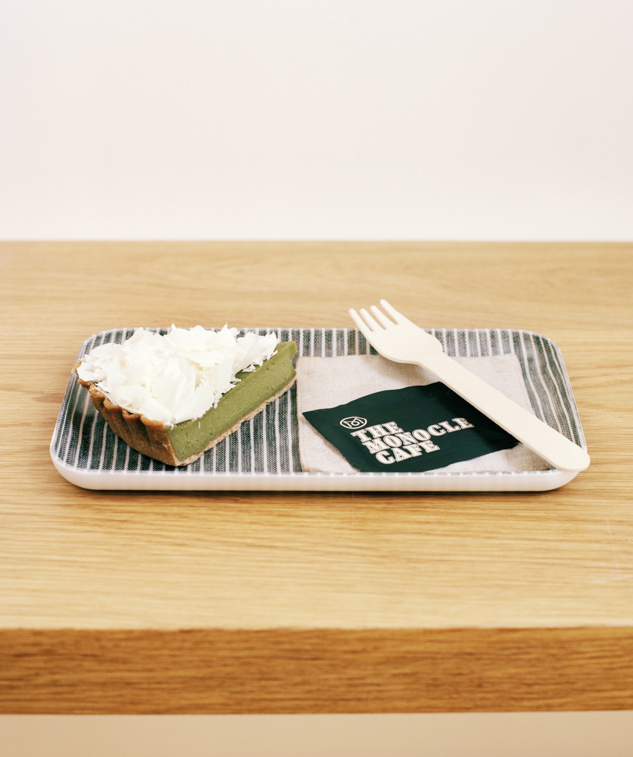 Lanka green tea cake with cream topping served on a striped Fog Linen tray with white fork and Monocle Café napkin.