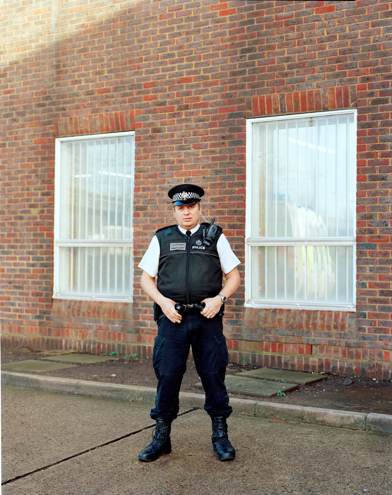 Police constable in uniform standing in front of brick building with white windows.