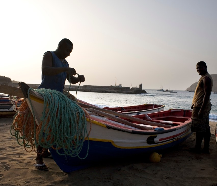 Fishermen with fishing nets and colorful boats on Tarrafal beach, Santiago, Cape Verde.