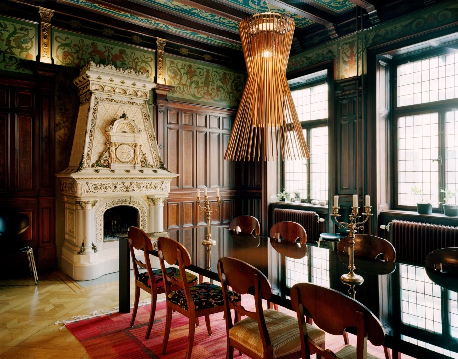 Ornate dining room with decorated ceiling, ceramic fireplace, wooden chairs, and woven pendant light.