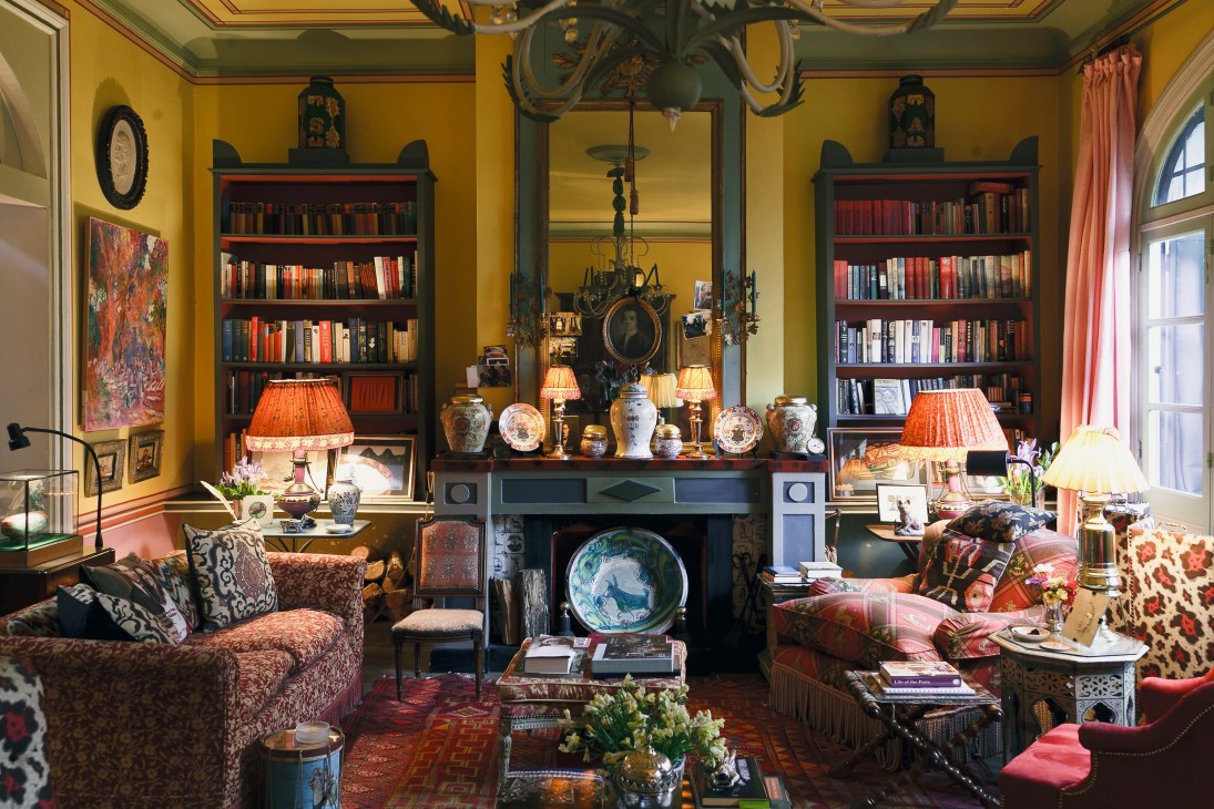 An ornate living room with yellow walls, bookshelves, fireplace, and eclectic furnishings in a former artist's studio.