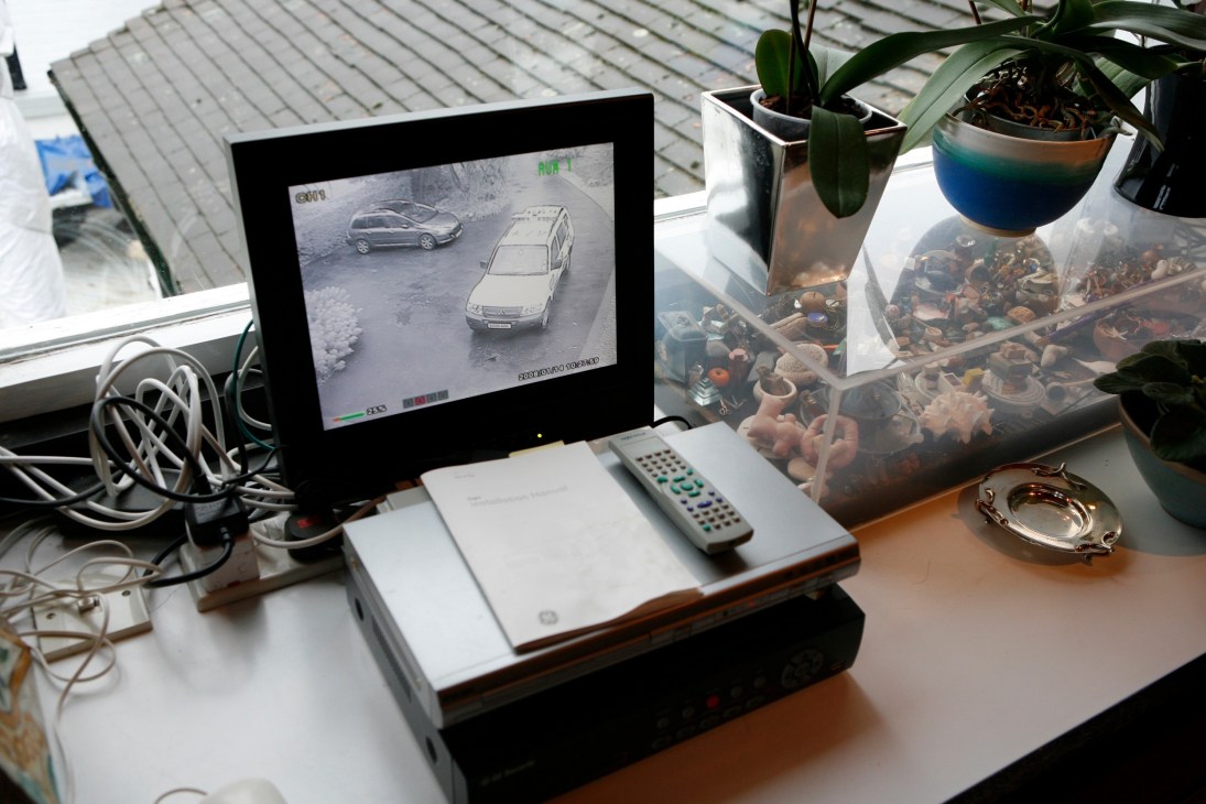 CCTV monitor displaying parked cars on a residential desk with plants and remote control.