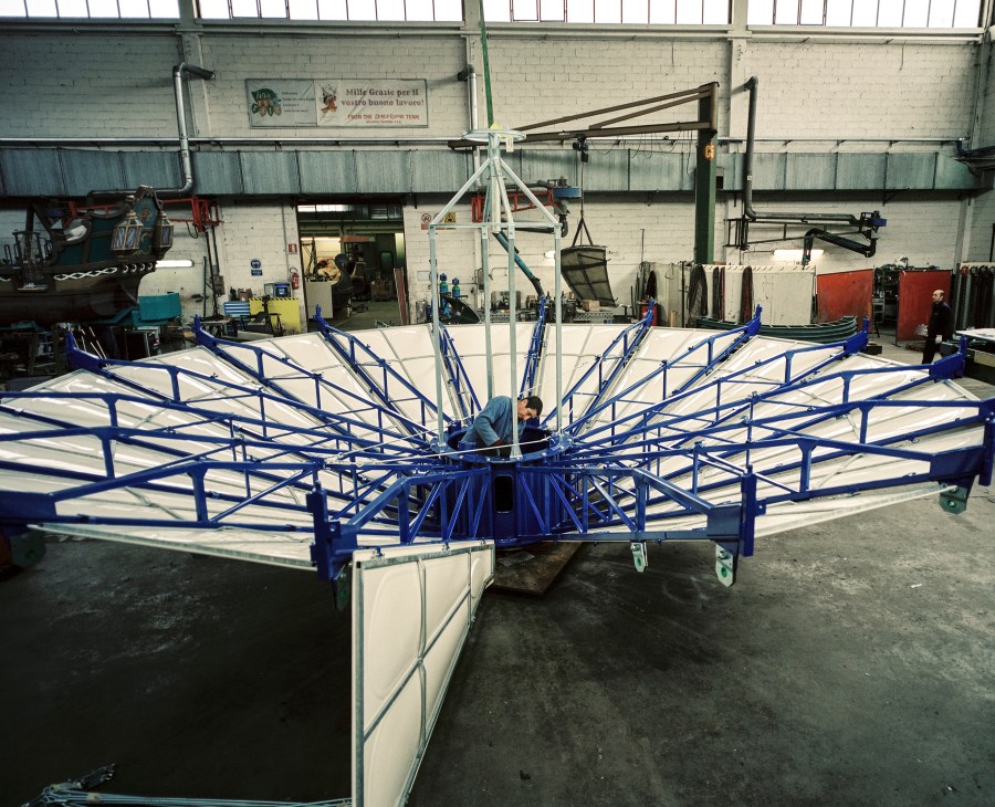 Worker painting a blue and white flying saucer ride frame in the Zamperla factory.