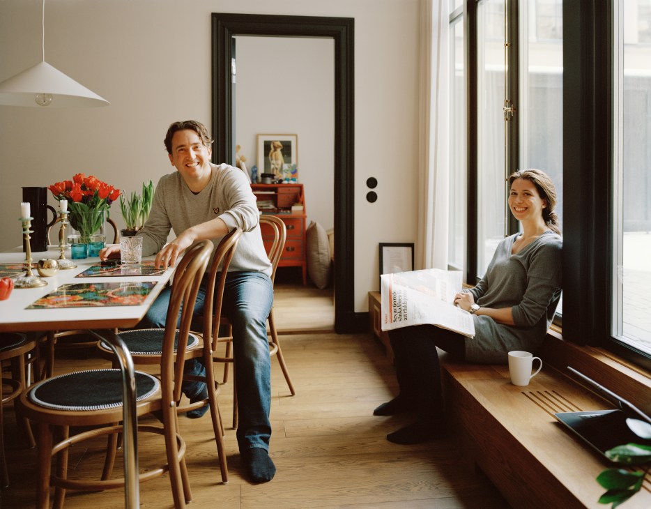 Rickard Billing and Sarah Feinberg in their Hat Factory apartment with wooden dining table, flowers, and large windows.