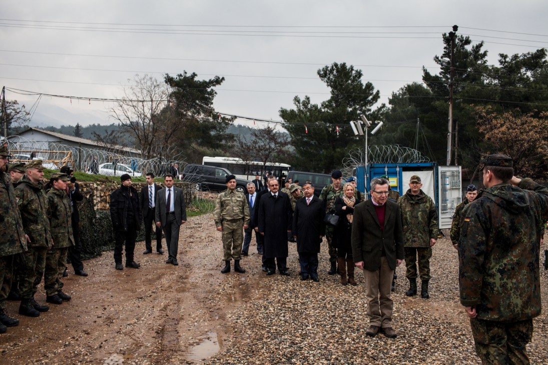 German defence minister Thomas de Maizière inspects troops at military base with soldiers and officials.