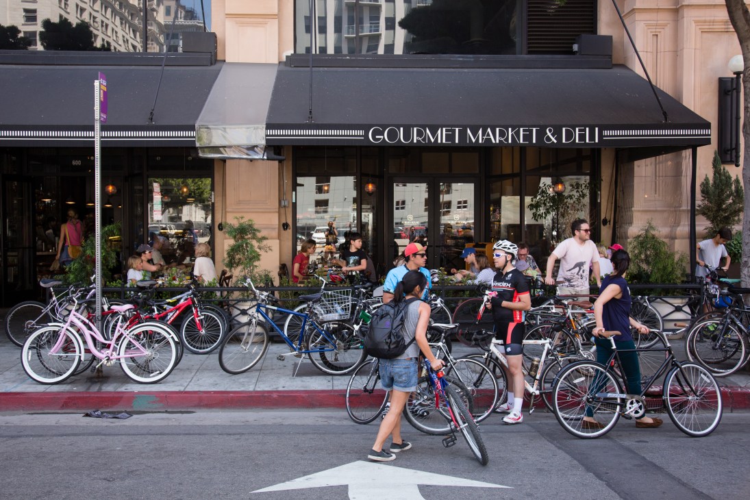 Cyclists gather on a downtown LA street outside a gourmet market and deli during CicLAvia.