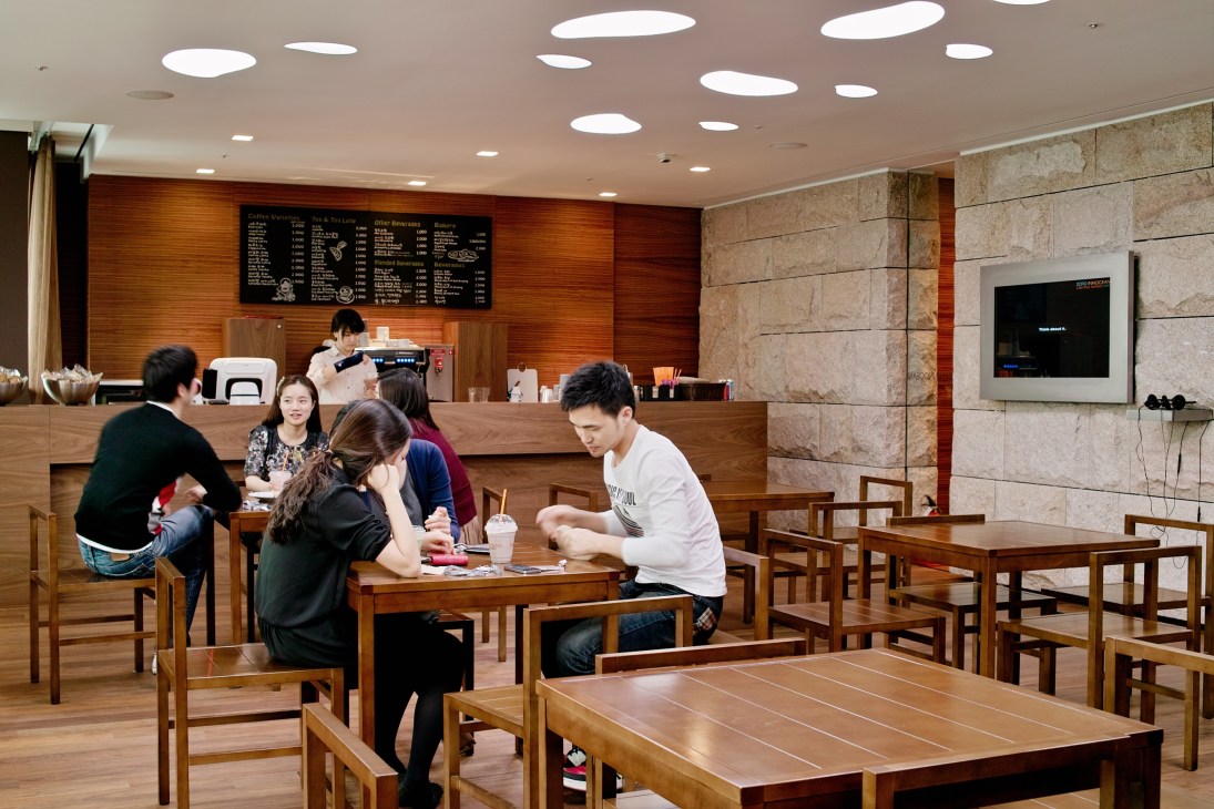 Modern café-style staff lounge with customers seated at wooden tables and a walnut counter with menu board.