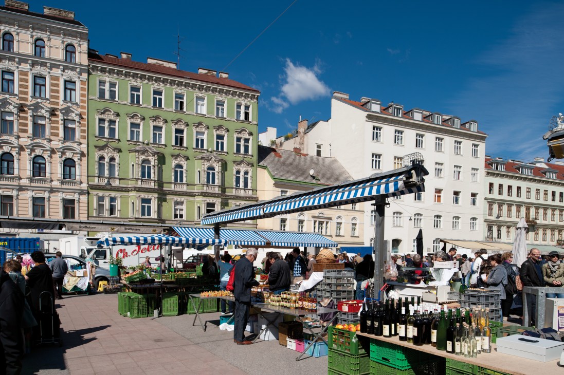 Karmelitermarkt outdoor square with vendors, blue-striped market canopies, and colorful Gründerzeit buildings.
