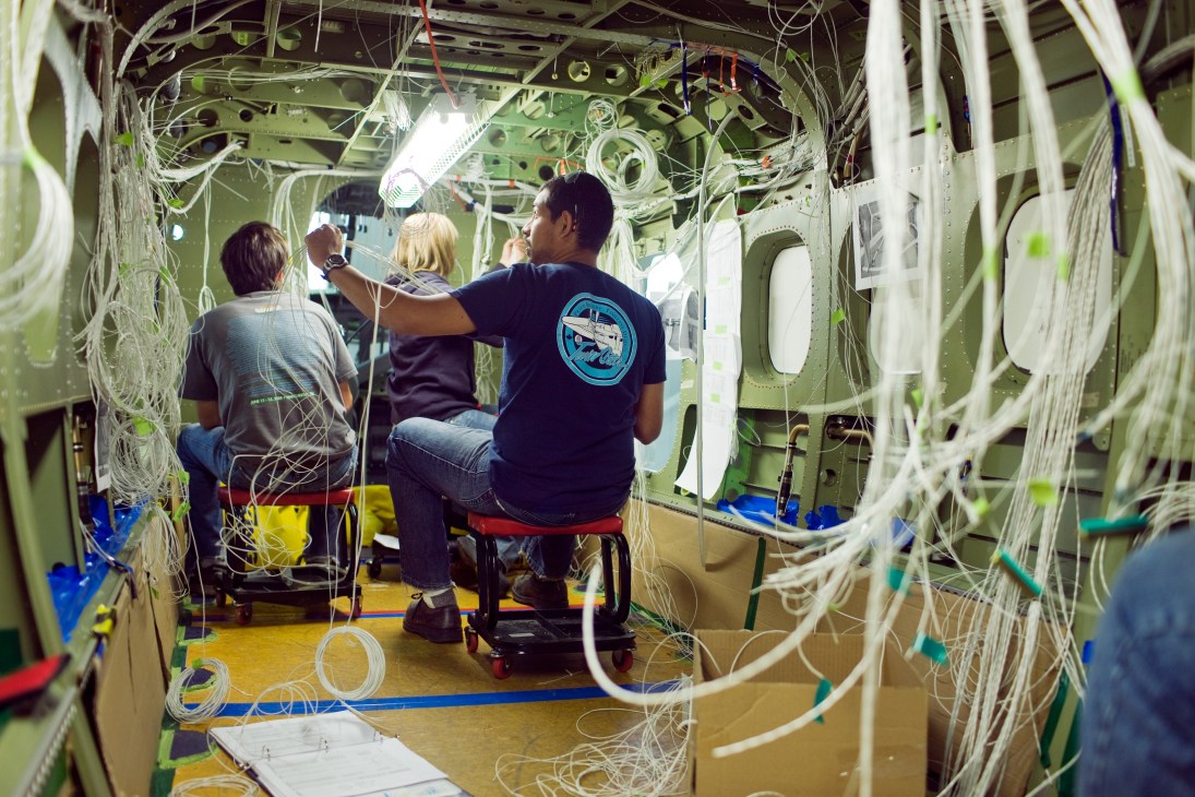 Viking Air employees stringing wires through the chassis of a Twin Otter aircraft.