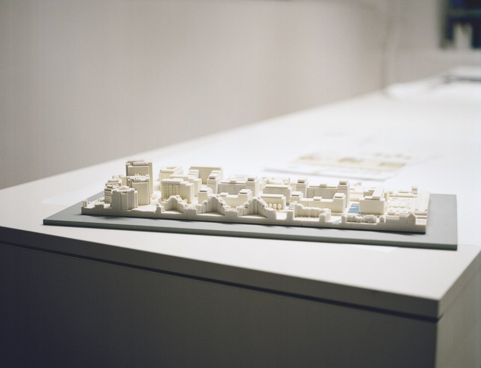 Architectural scale model of a city skyline with white buildings on a dark base displayed on a white table.