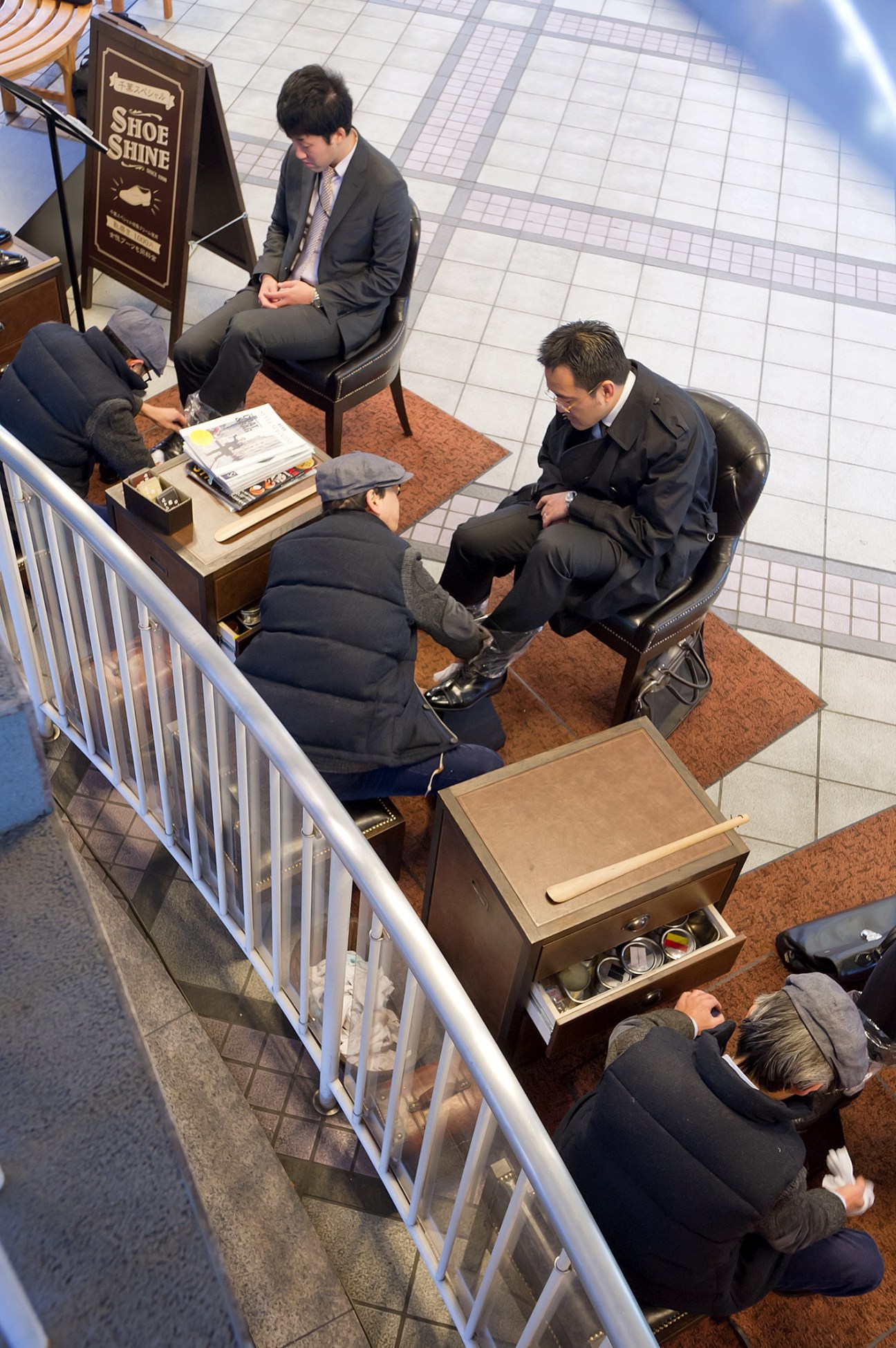 Overhead view of Mikoto Chiba's shoeshine shop in Tokyo with customers seated in leather chairs and staff attending to shoe service.