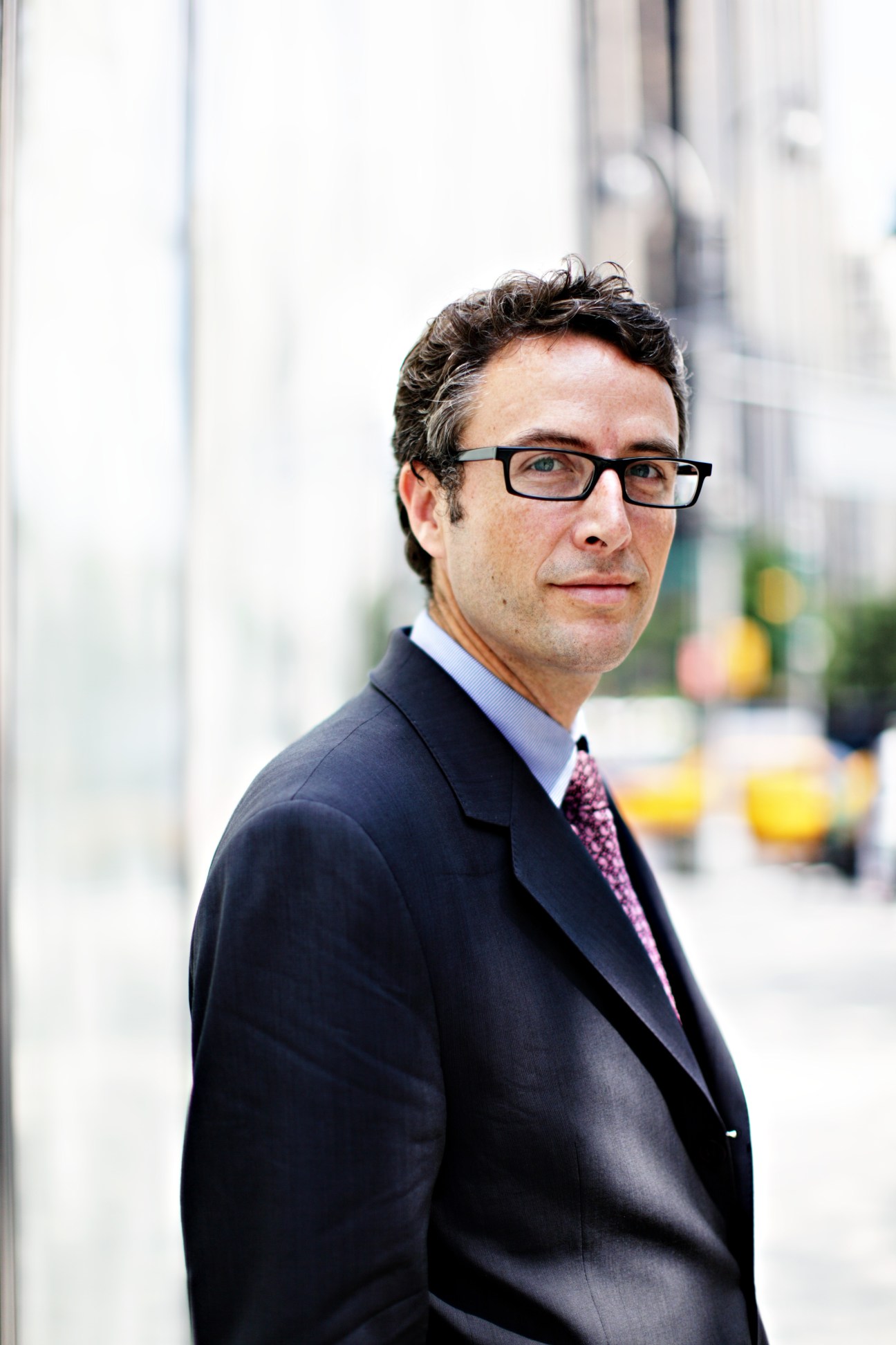 Man wearing glasses and dark blazer with purple tie on urban street