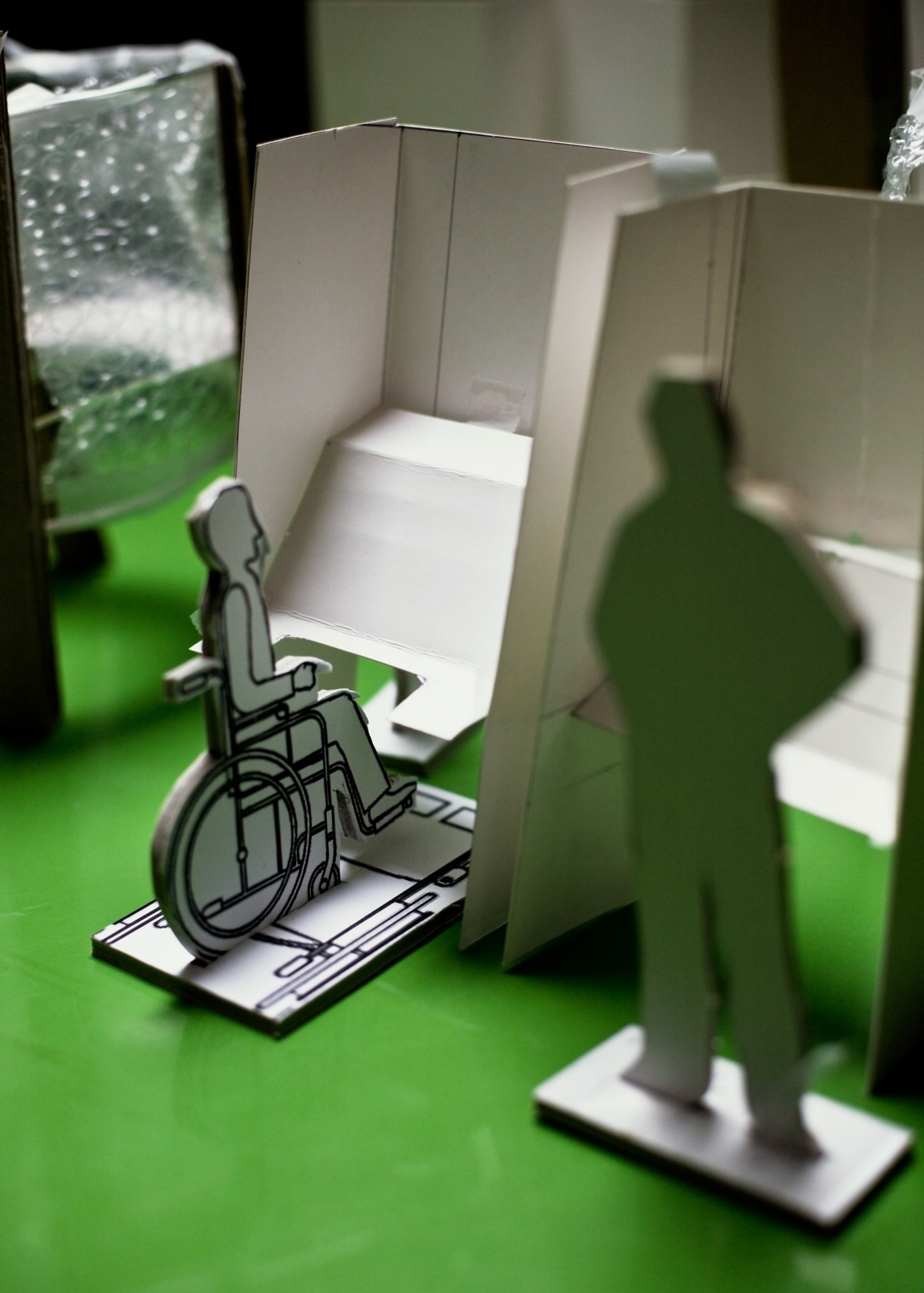 Model of an accessible voting booth with wheelchair ramp and writing surface on green display background.