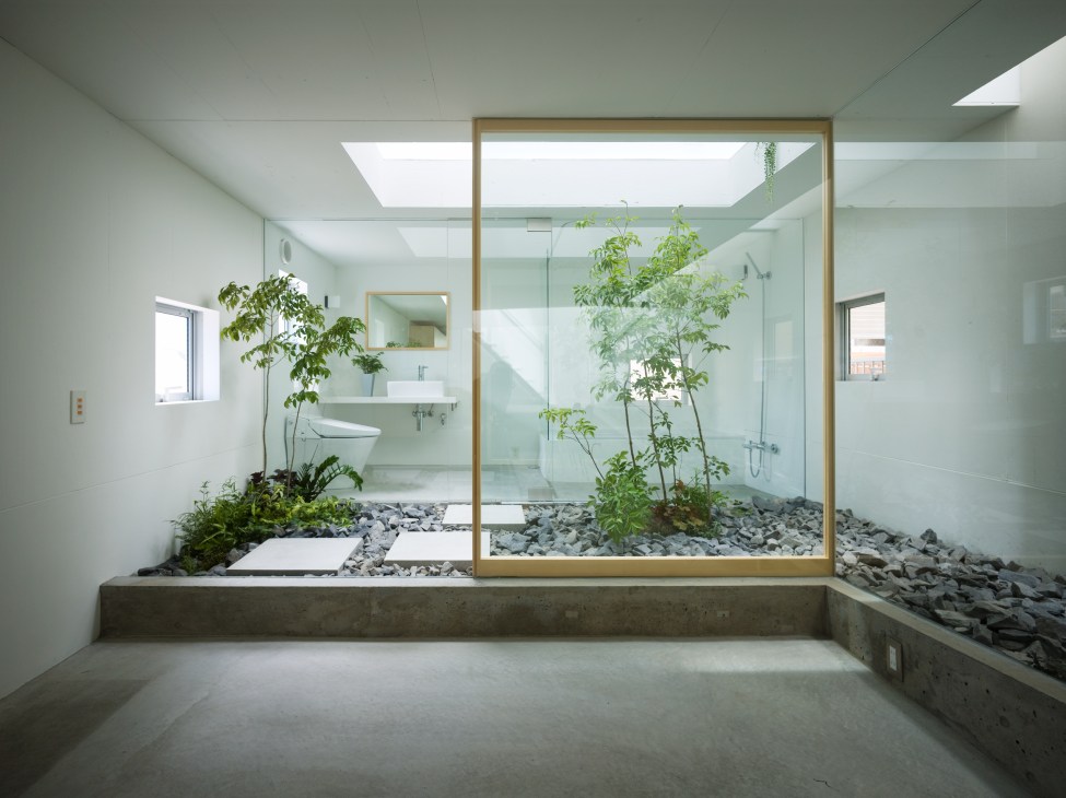 Modern bathroom with indoor garden courtyard featuring plants, coarse stones and glass enclosure.
