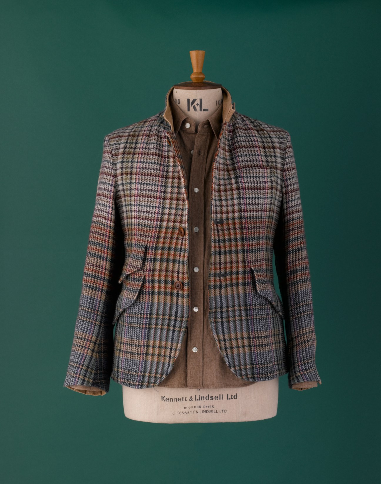 Multi-coloured checked tweed suiting jacket on a dress form against a teal background.