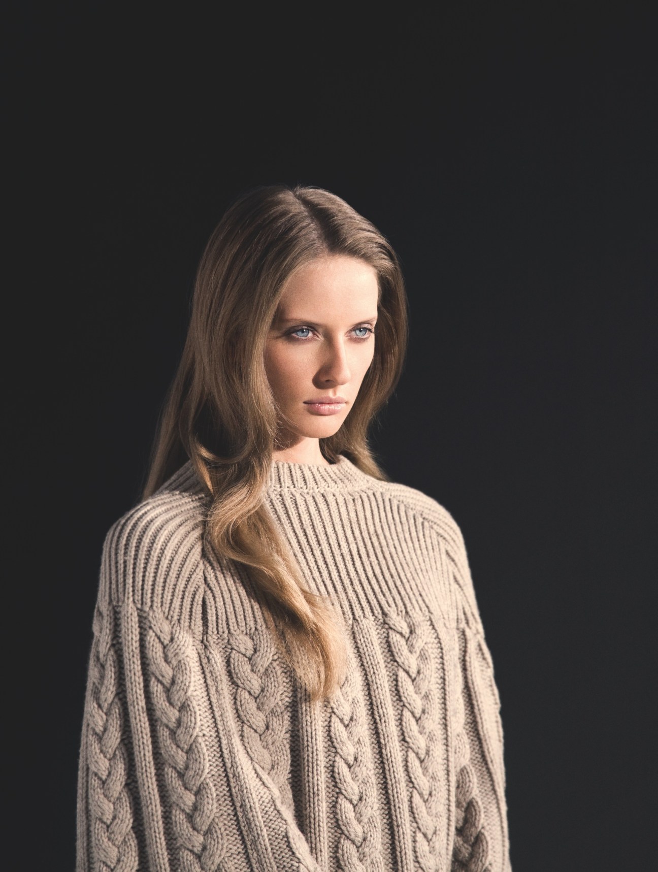 Model wearing a Louis Vuitton cape over a cream cable-knit sweater against a dark background.