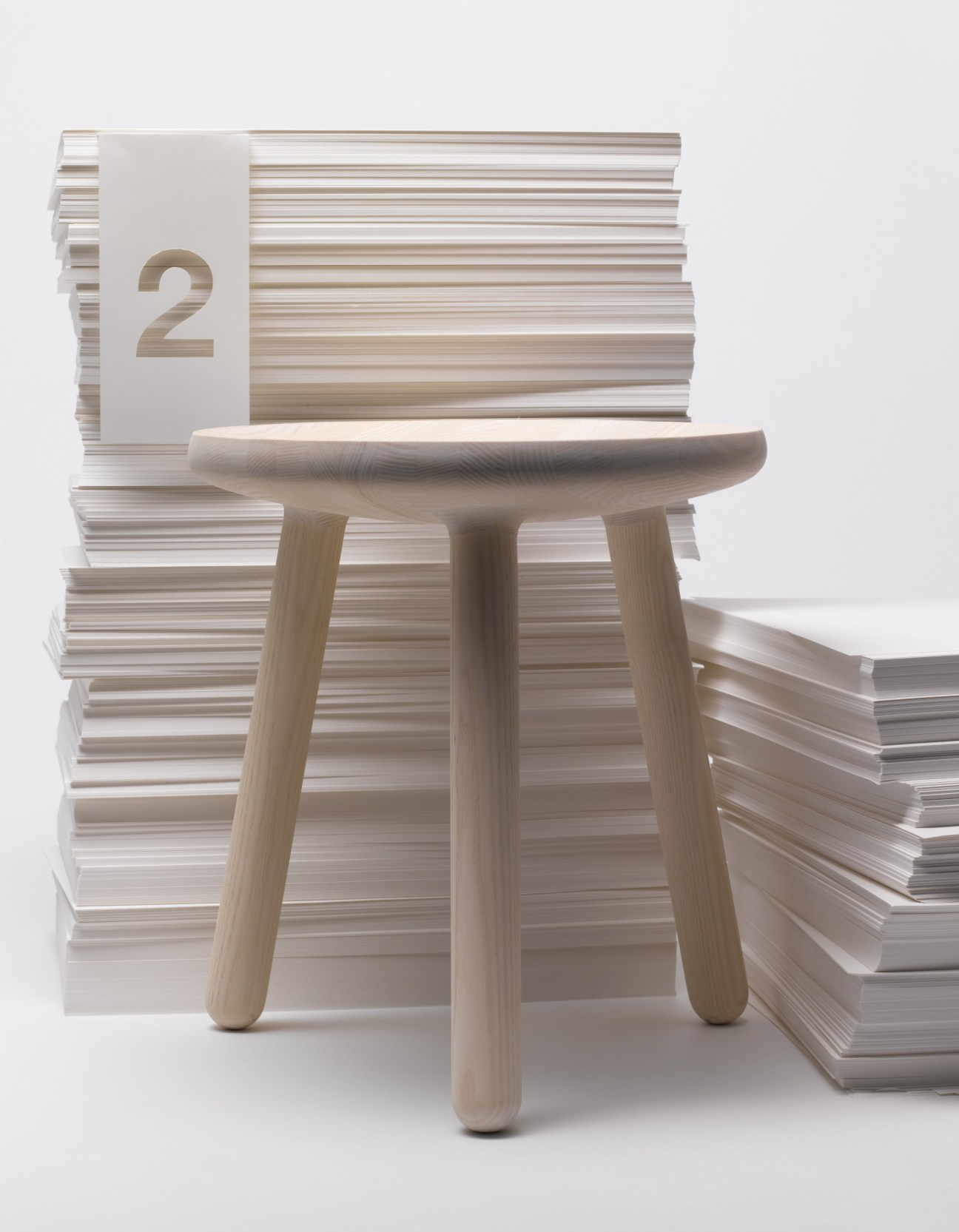 Staffan Holm three-legged ash wood milk stool surrounded by stacked white papers and notebooks.