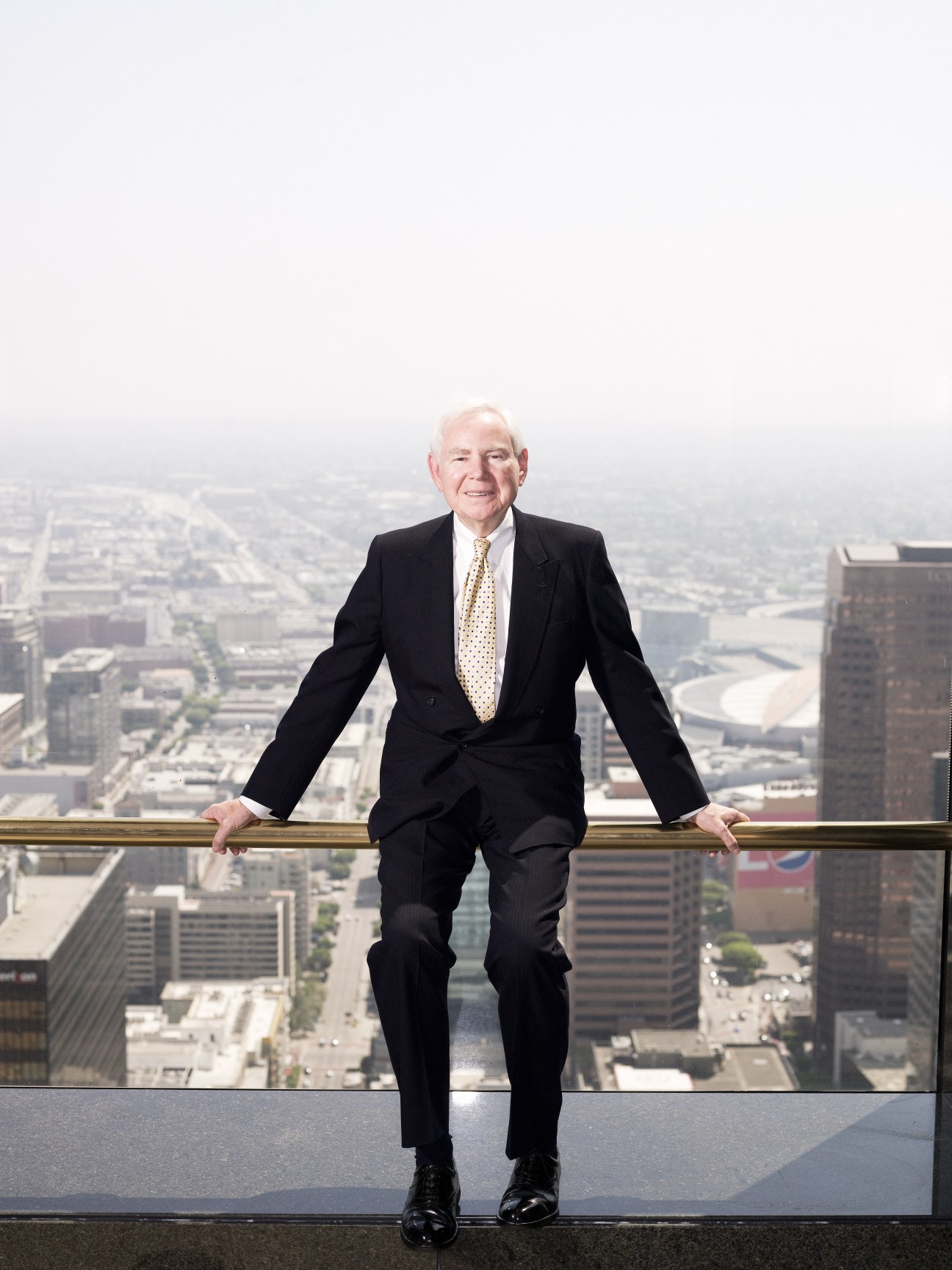 James A Thomas, CEO of Thomas Properties Group, poses on a high-rise balcony overlooking Los Angeles skyline.