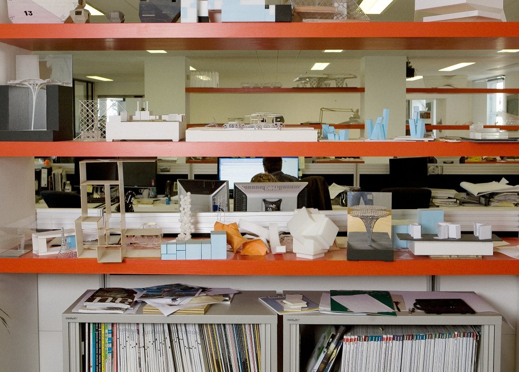 Shelves displaying architectural models and design materials in a modern office workspace with orange accents.
