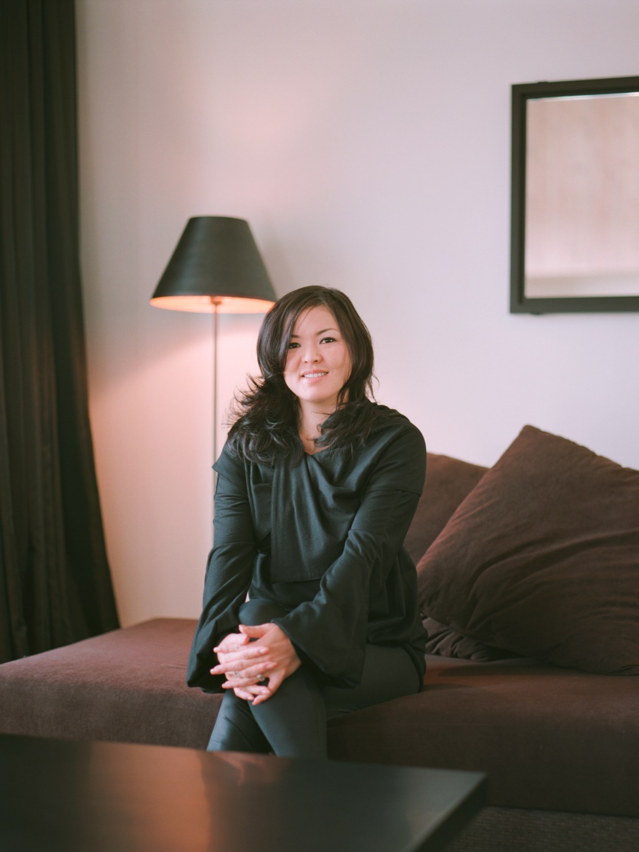 Atsuko Itoda, design partner at Riccardo Tossani, sitting on a brown sofa in a minimalist interior with a black floor lamp.
