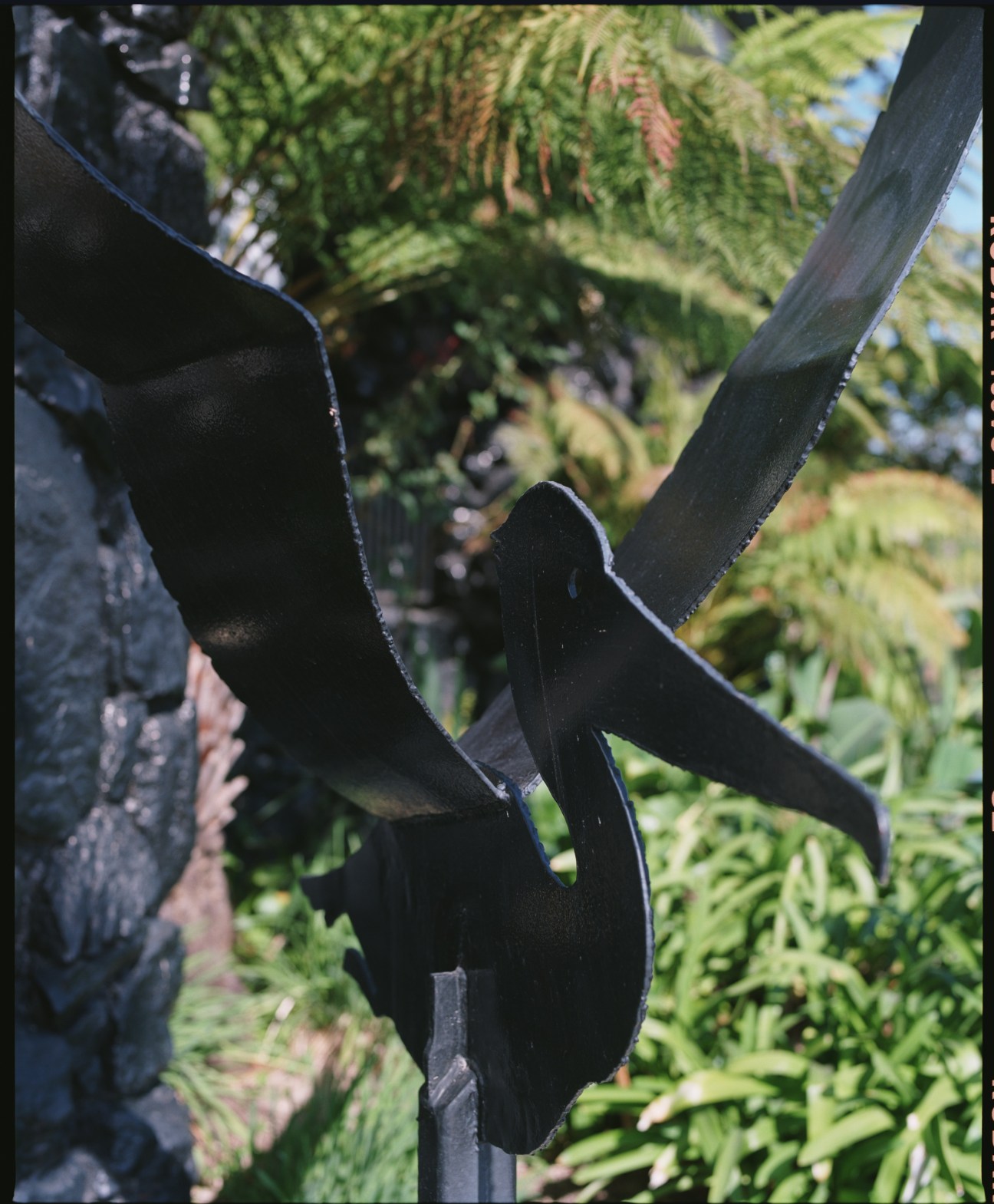 Close-up of a black pelican sculpture with foliage in the background.
