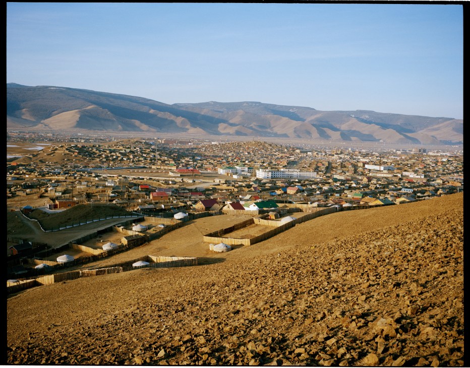Aerial view of Ulan Bator suburbs showing ger tented communities and houses spreading across a dusty valley with mountains in the background.