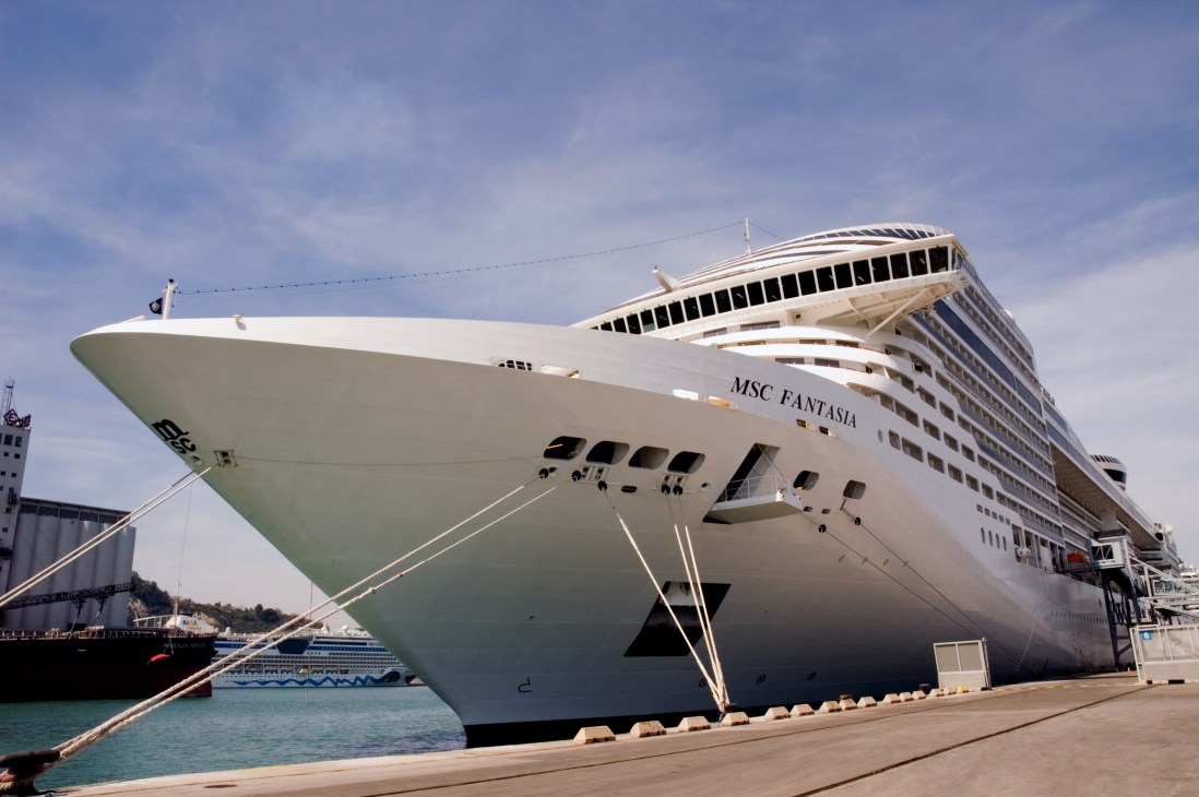 The MSC Fantasia cruise liner docked at a Mediterranean port with mooring lines secured to the dock.