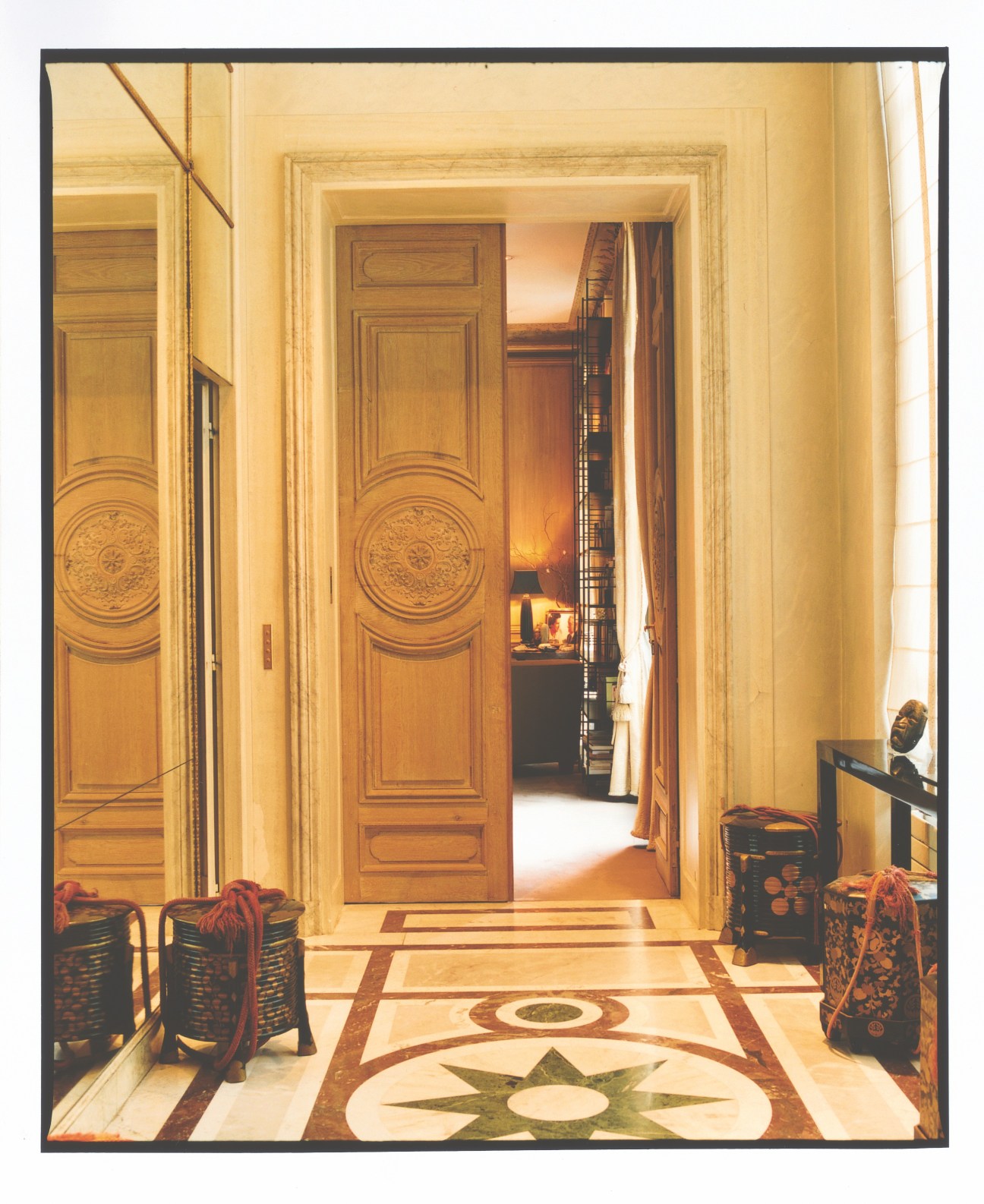 Elegant hallway with cream walls, ornate wooden doors, and inlaid marble floor in a Parisian apartment.
