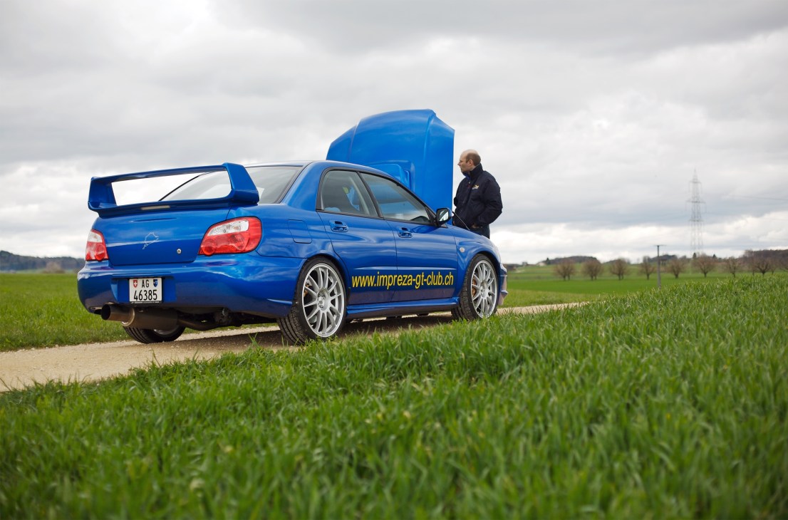Lawyer Lukas Ott stands beside his blue Subaru Impreza STI '03 in a rural field.