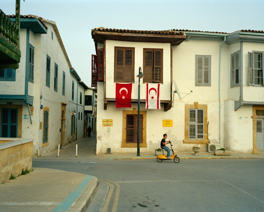 A street in Nicosia with traditional architecture and a Turkish flag hanging next to a TRNC flag on a cream-colored building.