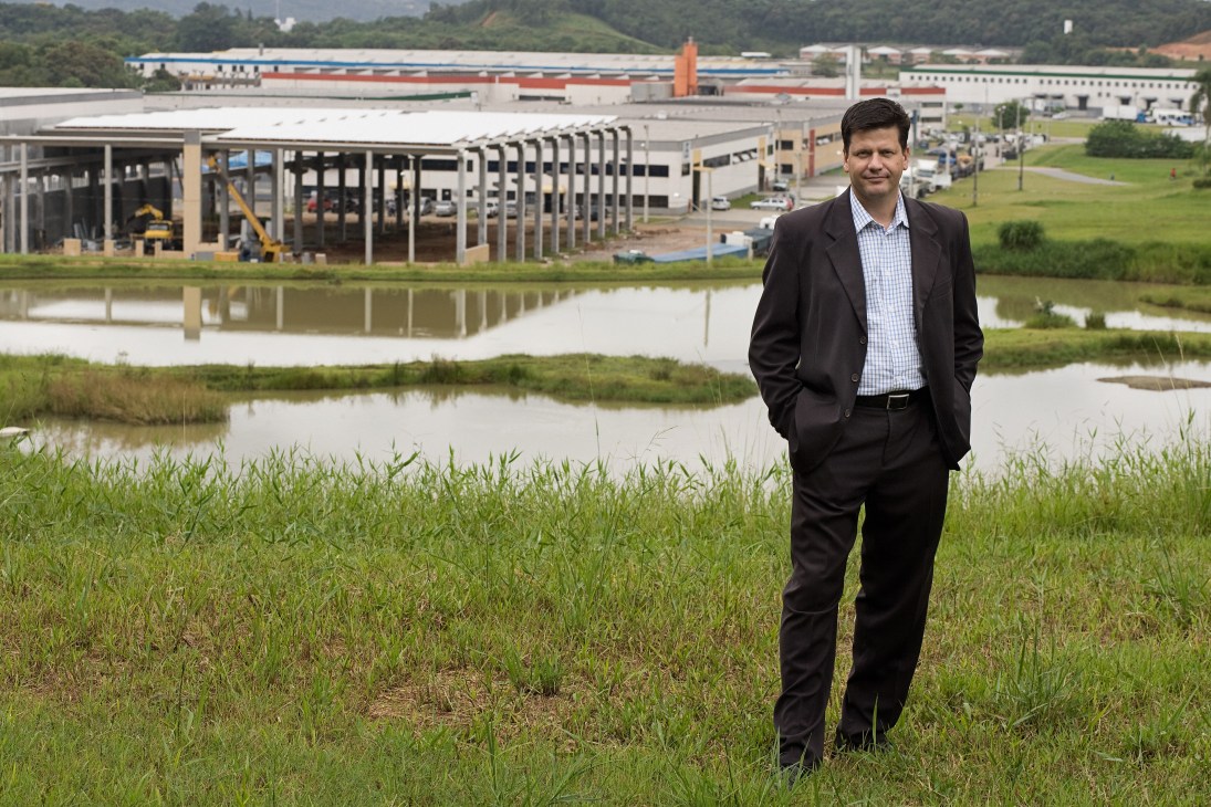Jonas Tilp, commercial director of Perini Business Park, stands in a field with industrial buildings and a pond behind him.