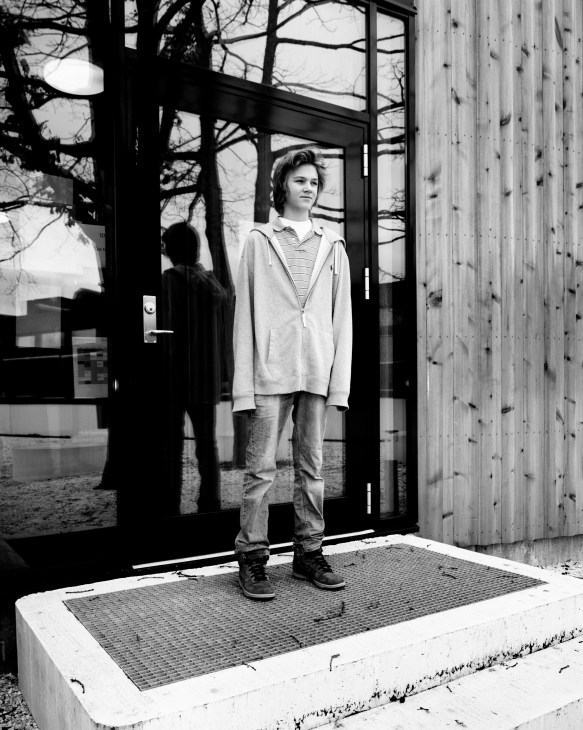 Black and white portrait of 14-year-old student Per Christian Wahlström standing in a modern school doorway with wooden cladding.