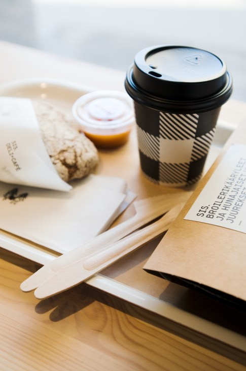Sis branded coffee cup with black and white chequered design on wooden table with pastry and napkins.