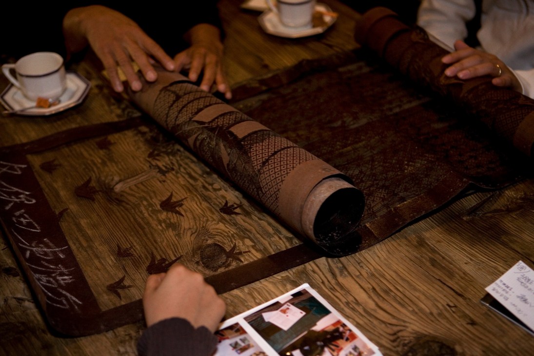 Hands examining hand-cut paper stencils rolled on a wooden surface with tea cups nearby.