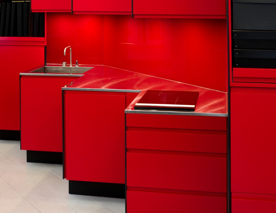 Red lacquered kitchen unit with stainless steel sink and Vola tap integrated into zigzag wall design.