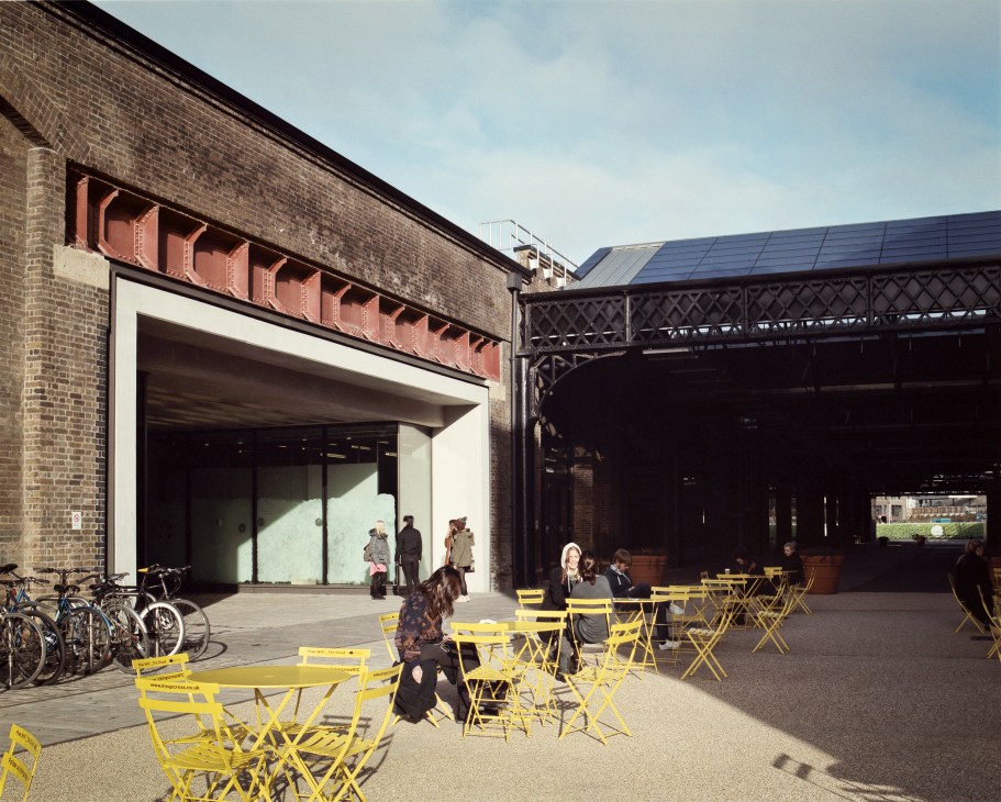 Students relax on yellow chairs outside a brick building with modern glass entrance at Central Saint Martins.