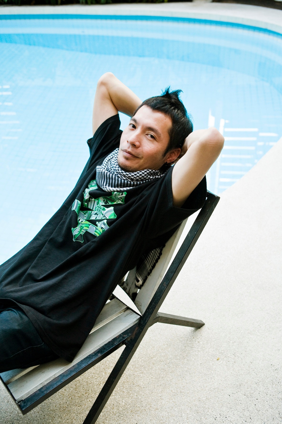 Man lounging in a black deck chair by a swimming pool.