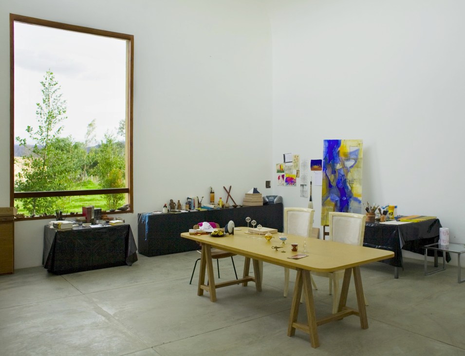 Artist's studio with wooden work table, art supplies, and large window overlooking countryside.