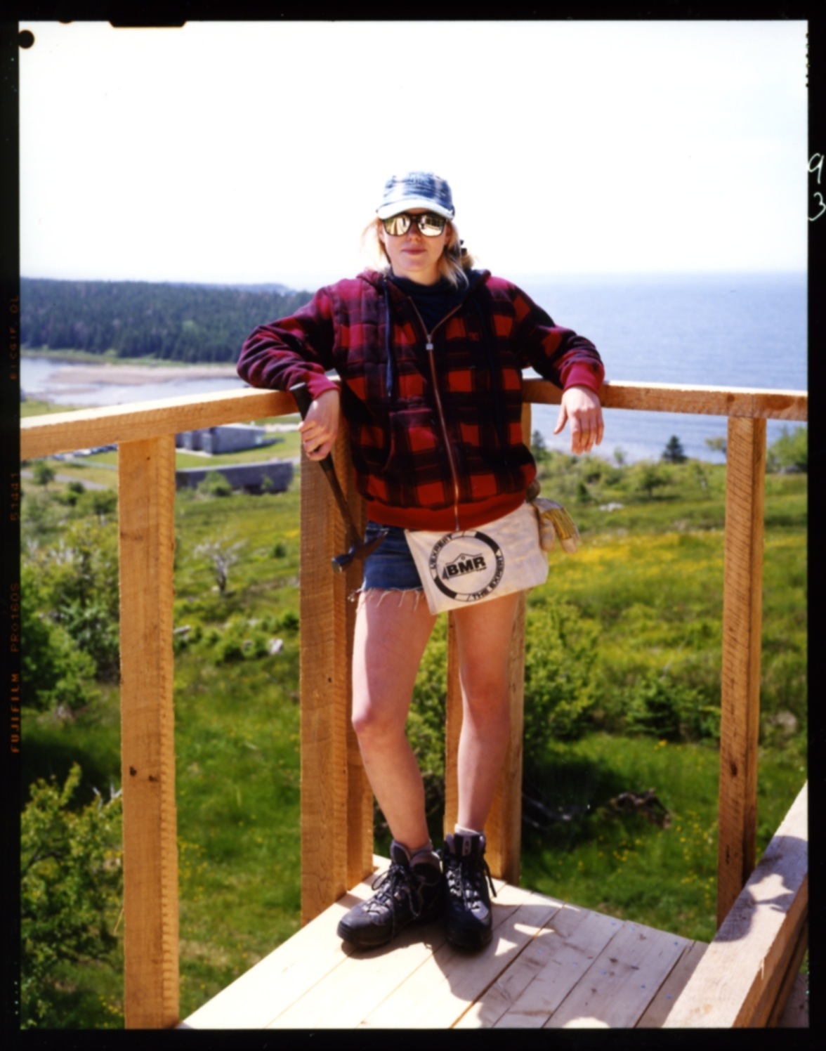 Student Maegan Magathan stands on a wooden deck railing overlooking a forested Nova Scotia landscape with water visible in the distance.