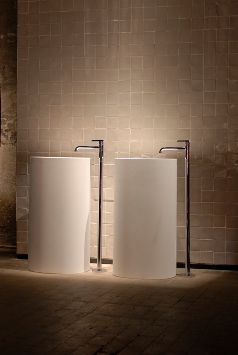 Two cylindrical white basin and bath fixtures with chrome fittings against a tiled wall.
