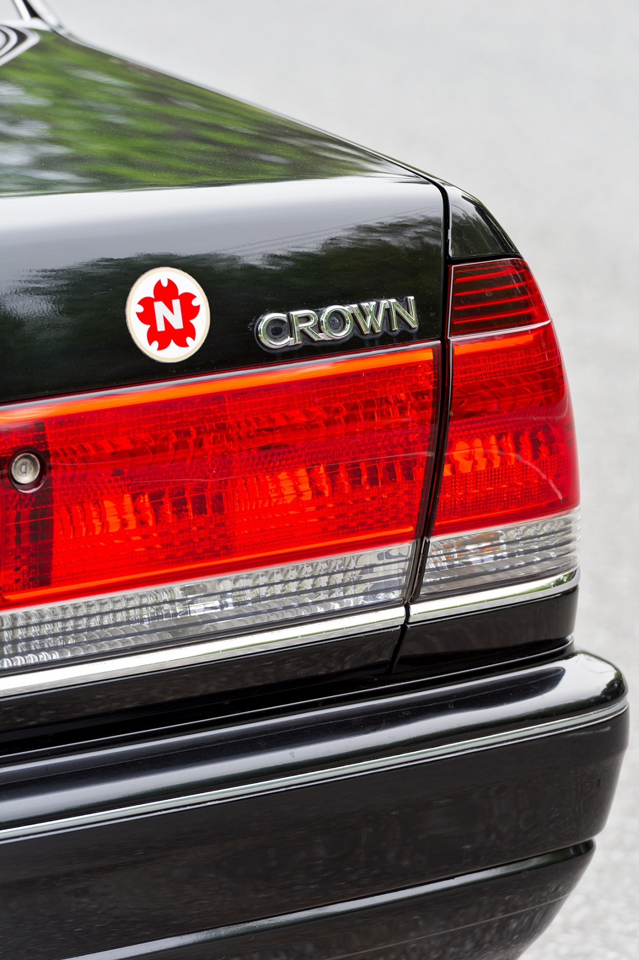 Close-up of a Toyota Crown taxi rear showing red taillights, Nihon Kotsu red logo, and Crown badging.