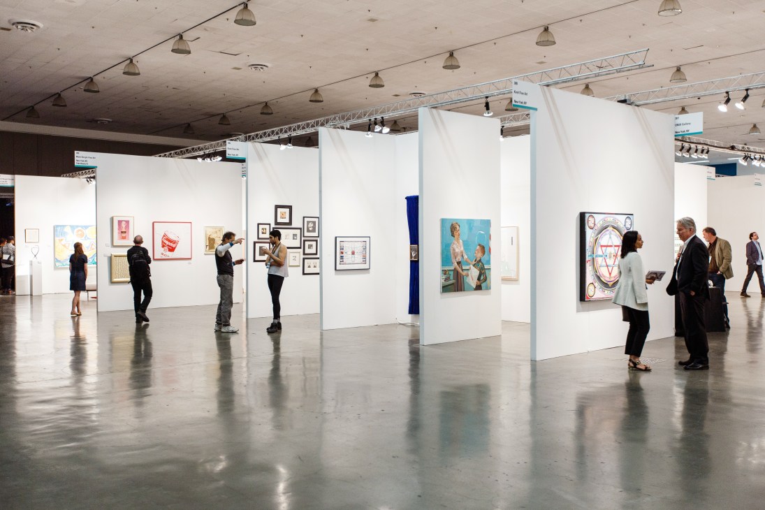 Visitors walk through white gallery booths displaying framed artworks at Silicon Valley Contemporary art fair.