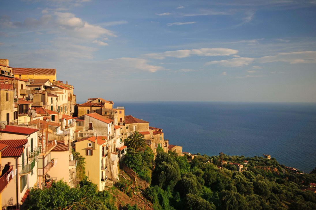 Colorful Italian coastal town with terracotta-roofed buildings cascading down hillside toward blue sea.