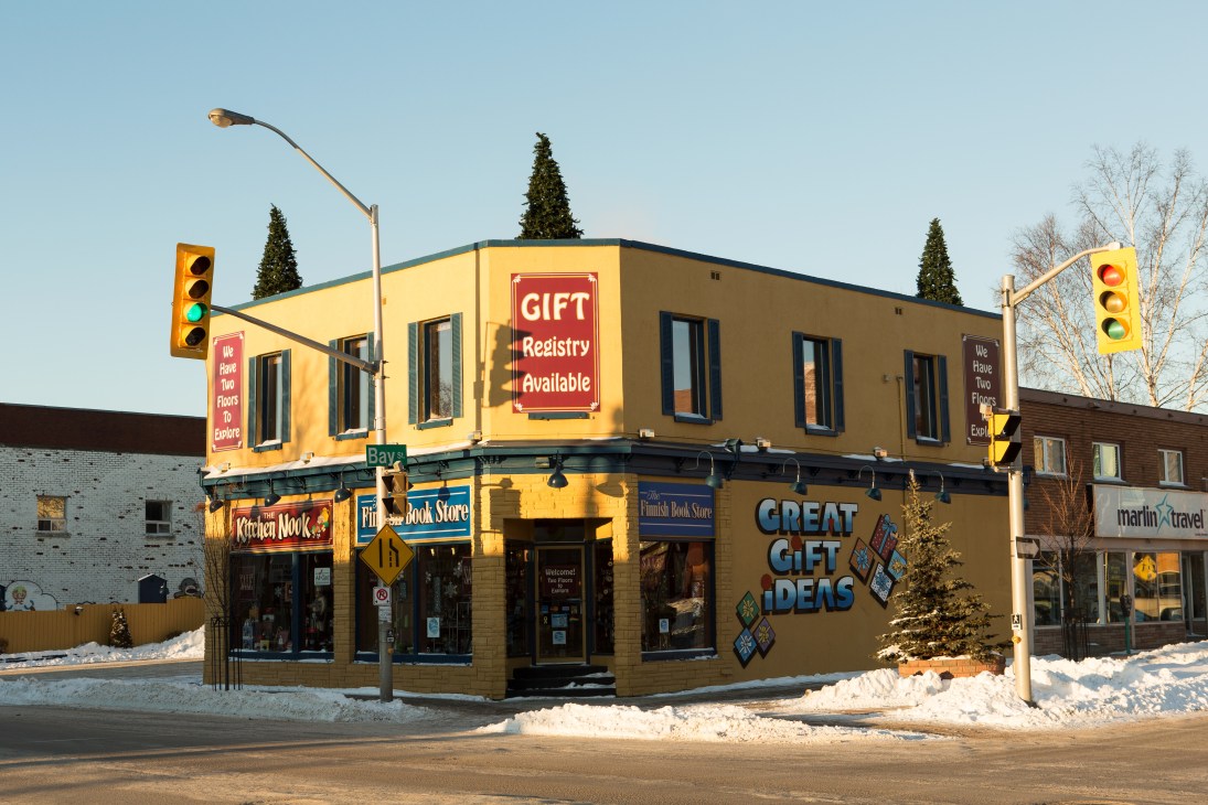 The Finnish Book Store, a yellow corner building in Thunder Bay with blue signage and snow on the ground.