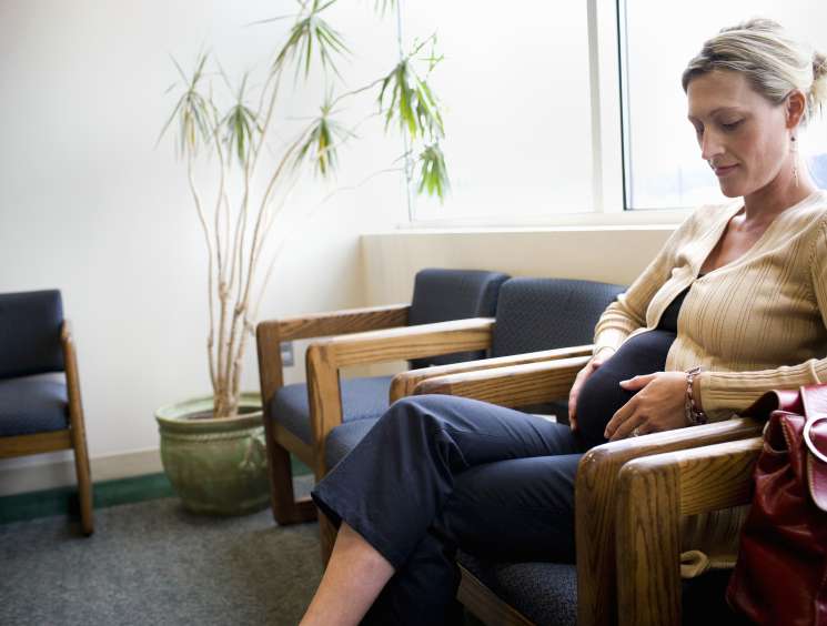Pregnant woman sitting in a waiting room chair with a potted plant nearby.